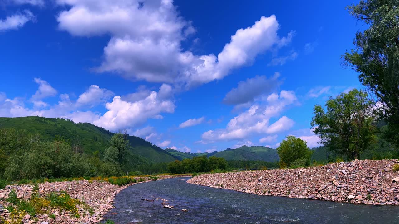 A Tranquil River Meandering Through Lush Green Mountains Under a Vast Blue Sky with Fluffy Clouds, Capturing the Serene Beauty of Nature in a Peaceful Landscape