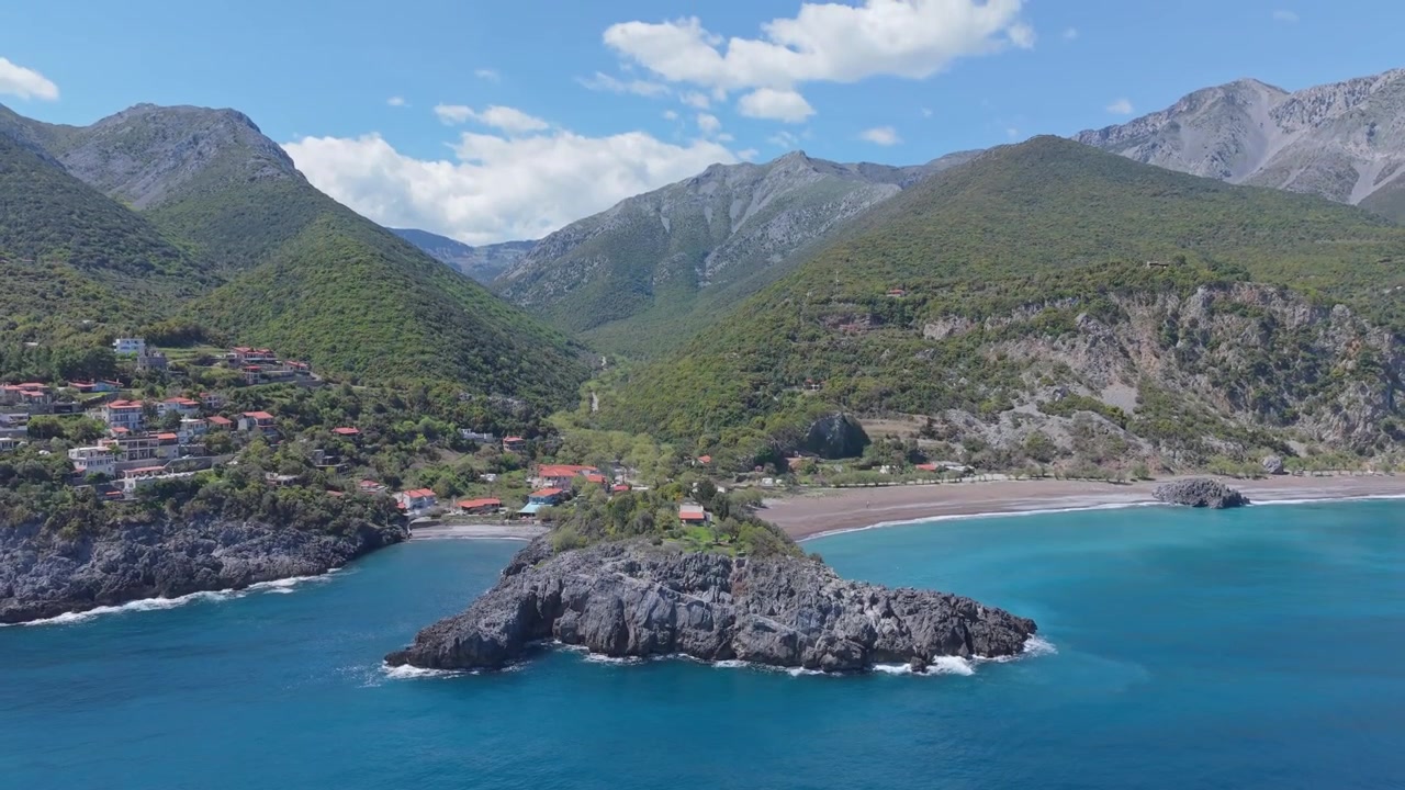 Recuo de drone de cima para baixo com uma inclinação suave para cima, revelando a costa rochosa, águas cristalinas e a vibrante paisagem natural que cerca a Praia de Limnionas na Ilha de Evia, Grécia.