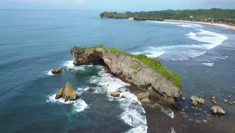 vista de drones de la costa con una enorme roca de coral con racimos de pequeñas rocas que aplastan la ola en la playa tropical