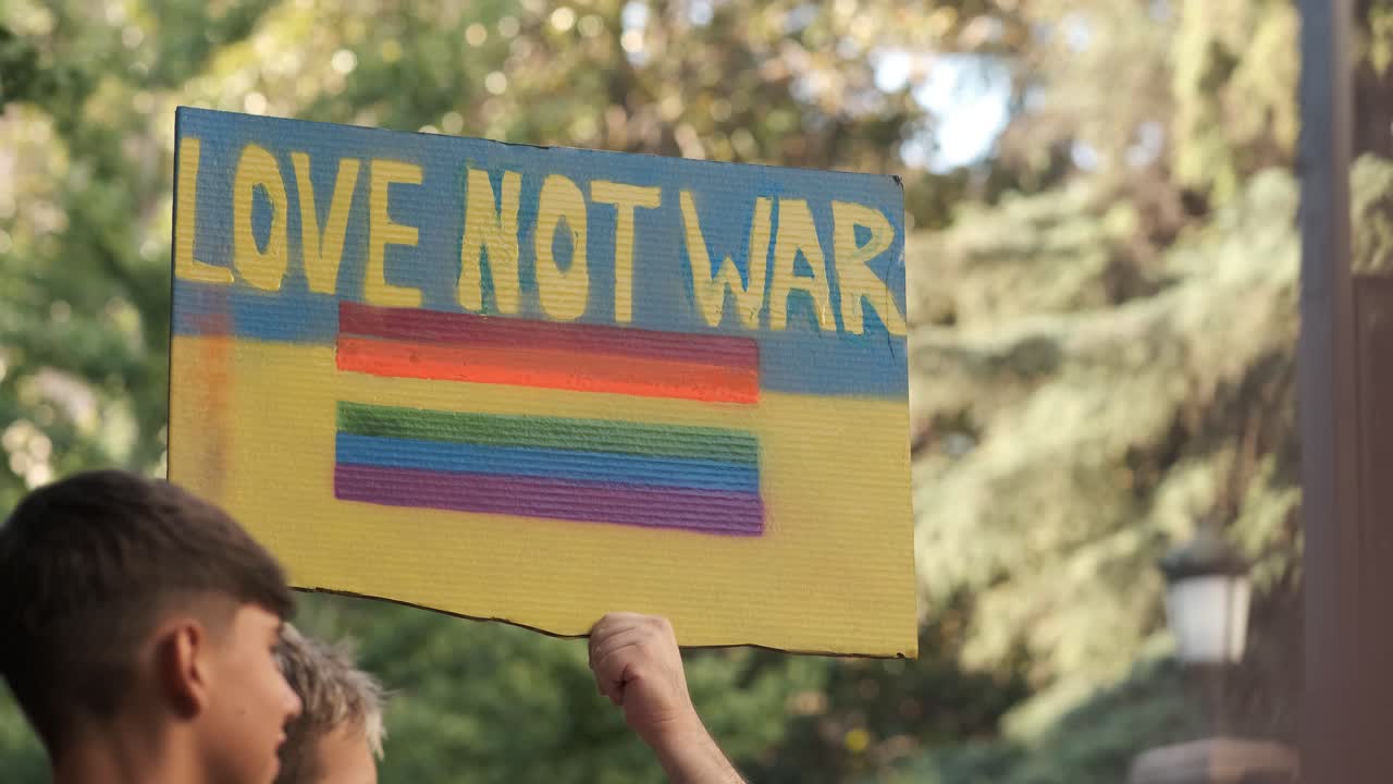 GRANADA, SPAIN - JUNE 28, 2022: People at the pride manifestation, Ukrainian yellow blue flag in hand with text LOVE NOT WAR