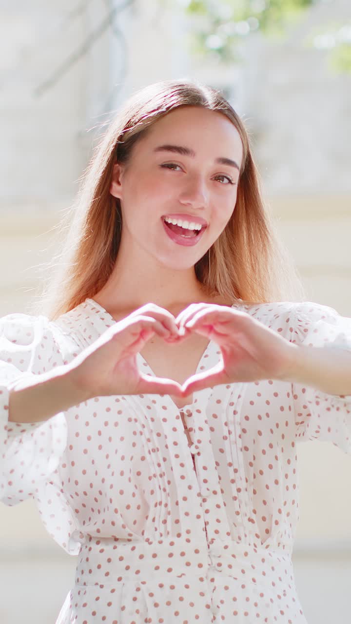 백인 여성은 사랑의 상징을 만니다. 카메라에 심장 기호를 보여주고, 만적인 감정을 표현합니다.