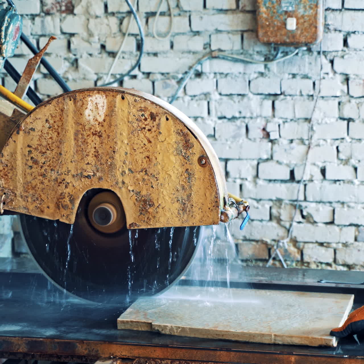 Man worker is putting stone slab into the CNC machine in factory. Automated machine for cutting stone slab. Running water for cooling while sawing the stove indoors.