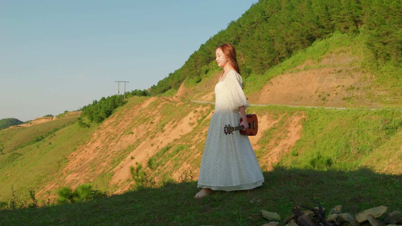 barefoot woman girl in white long dress walking and dancing in slow motion carrying acoustic ukulele guitar