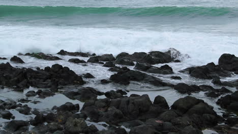 close-up view of rocks offshore crashed by strong sea waves and reflecting on and across stones during the day in nromla speed motion capture at 24fps