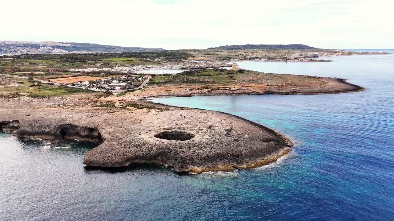 A Lagoa de Coral Il-Qarraba em Mellieħa, Malta, revela um sumidouro cárstico circular em Calcário Coralino Superior dentro de um planalto costeiro acidentado perto da Baía de Armier e do Canal de Comino, em uma tomada aérea de drone em órbita lenta.