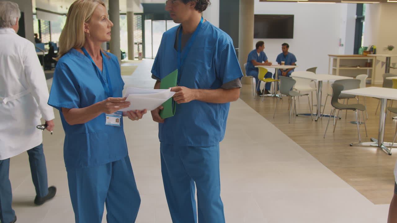 Sundhedspersonale i scrubs diskuterer patientjournaler ved uformelt møde på travlt hospital