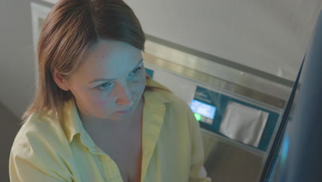 high angle view shows female technician in laundry operating payment screen, finger presses buttons on operator machine, focused workflow, bright room, modern service process, cashless control