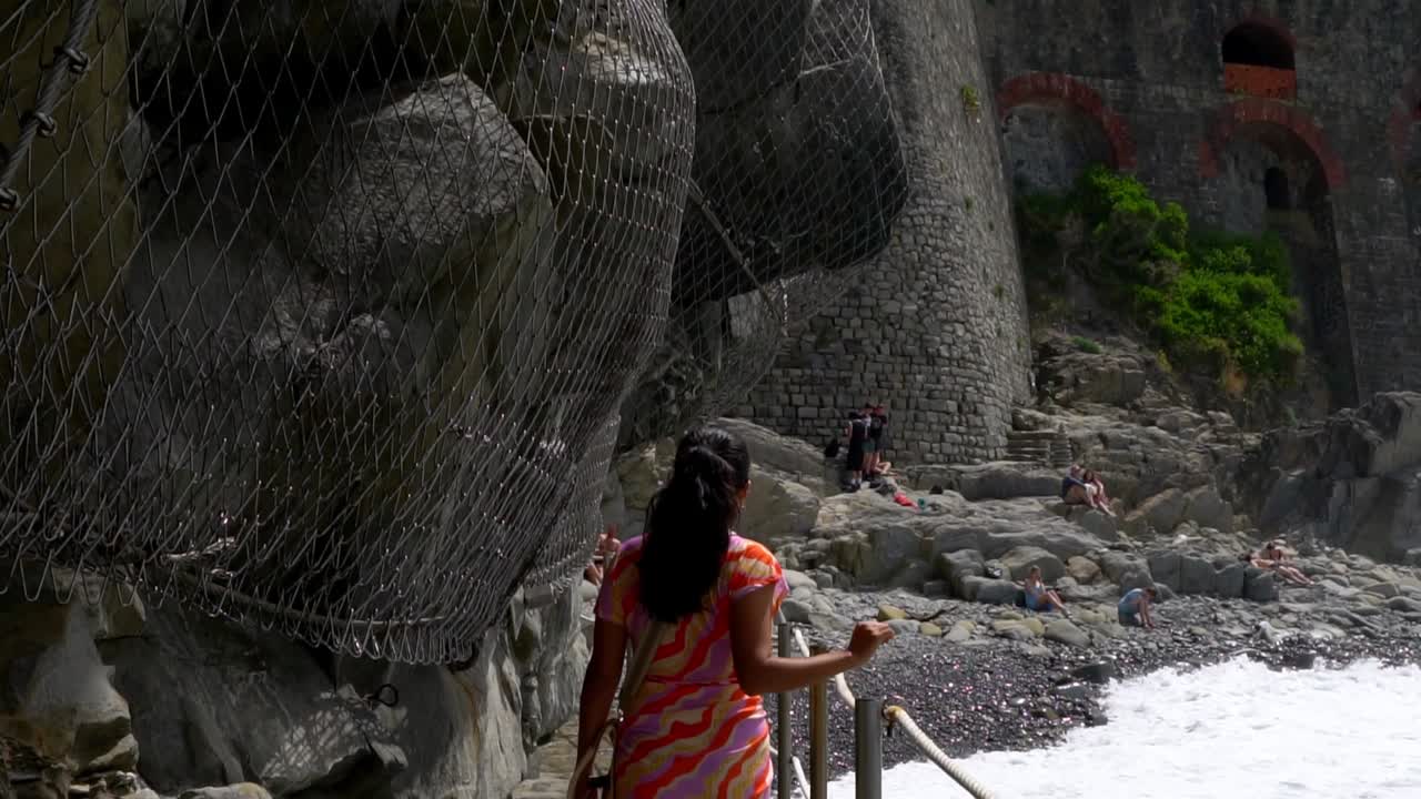 A Woman Is Walking On The Trails Near Stony Beach At Riomaggiore Village In The Cinque Terre Region Of Italy. Slow Motion Shot