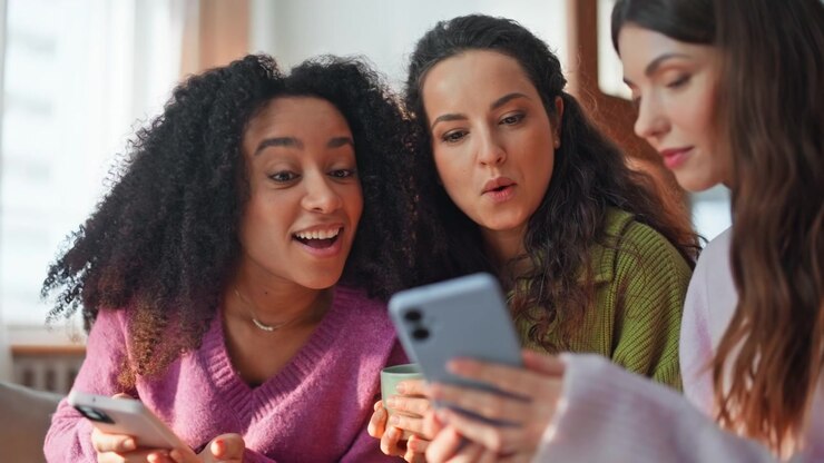Three friends scrolling smartphones sitting couch home closeup. Positive women