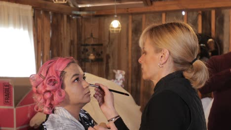 pink haired asian model looks at professional hair and makeup artist applying concealer - concentration and focus - 23.98fps