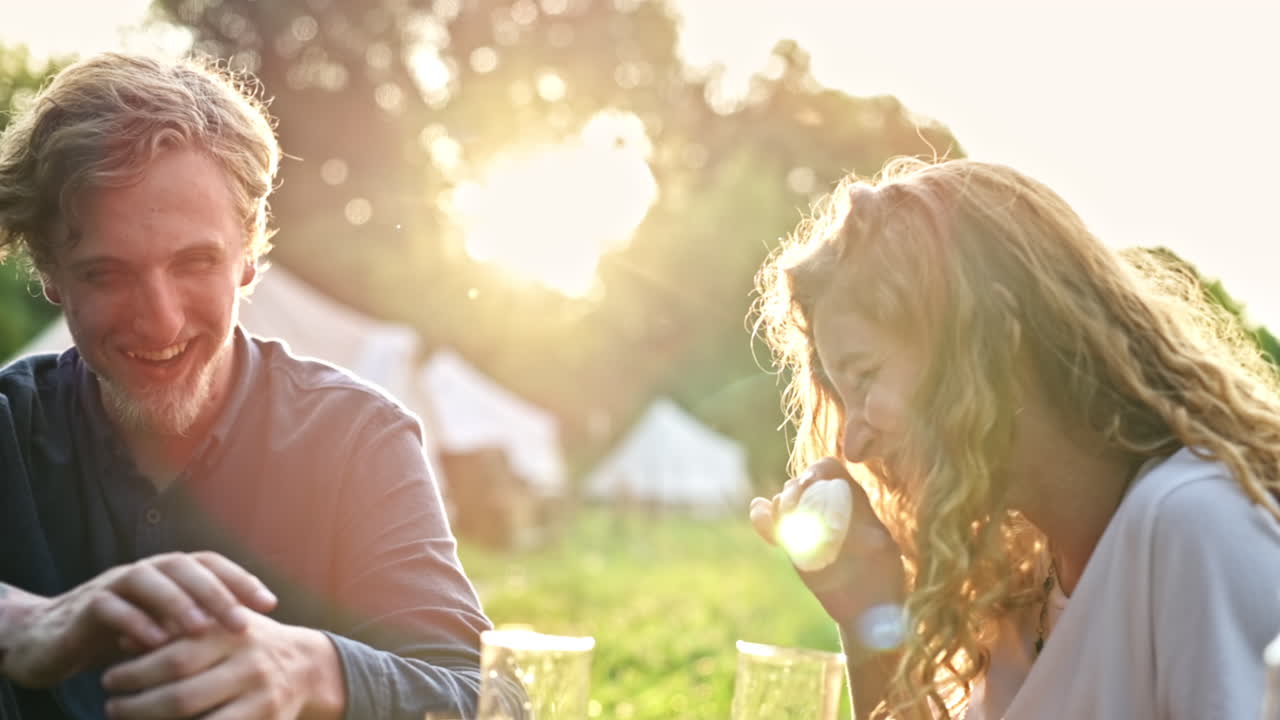 A couple having breakfast in the nature at glamping. Drinks, food, talking and smiling. Tent on the background. Slow motion
