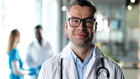 retrato de un médico caucásico con un vestido blanco y gafas mirando a la cámara, sonriendo y de pie en la clínica