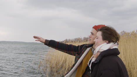 Side-View-Of-A-Teenage-Boy-And-Teenage-Girl-Talking-Standing-Near-Of-Seashore-On-A-Cloudy-Day,-Boy-Show-Something-With-His-Arm