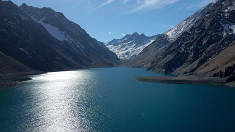 Boom-Up-Vista-Aérea-De-La-Laguna-Del-Inca,-Chile-Con-Montañas-Cubiertas-De-Nieve-En-El-Fondo-En-Un-Día-Soleado