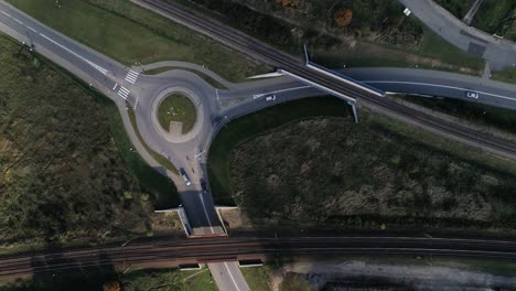 Círculo-De-Tráfico-En-Una-Calle-Plana-Con-Coches-Que-Pasan-Combinados-Con-Vías-De-Tren-Grabadas-Desde-Arriba-Desde-Un-Dron