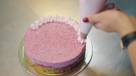 confectioner decorates cake with white cream from pastry bag