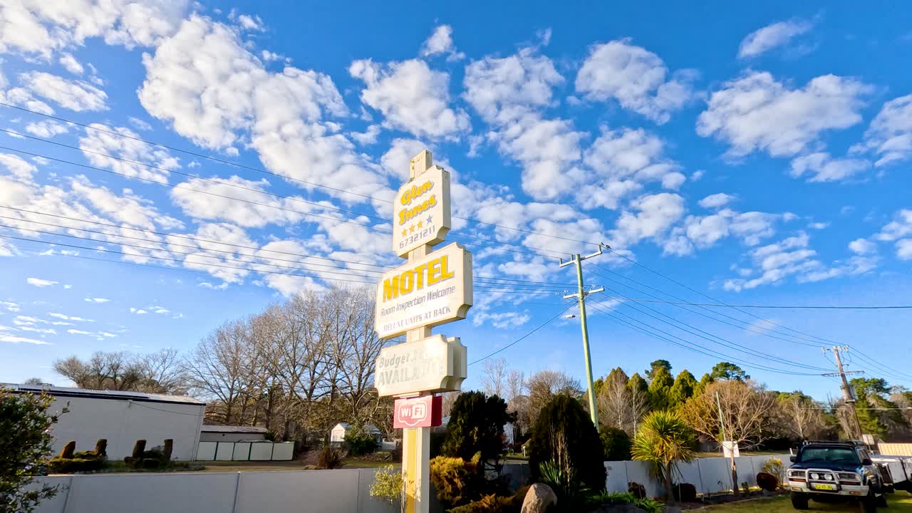 Una panoramica grandangolare rivela un'insegna di motel a bordo strada ed edifici in pieno giorno.