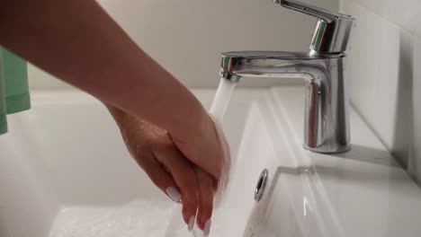 young female rubs bulms washing hands with tap water