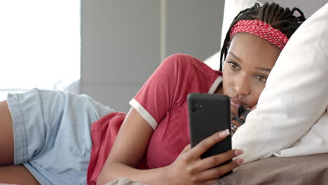 African-American-young-woman-lying-on-bed,-holding-smartphone