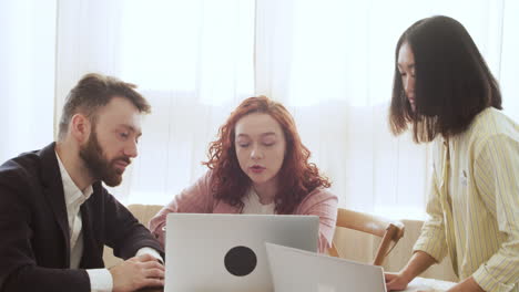 group of three multiethnic colleagues sitting at table and debating while looking laptop computer 2