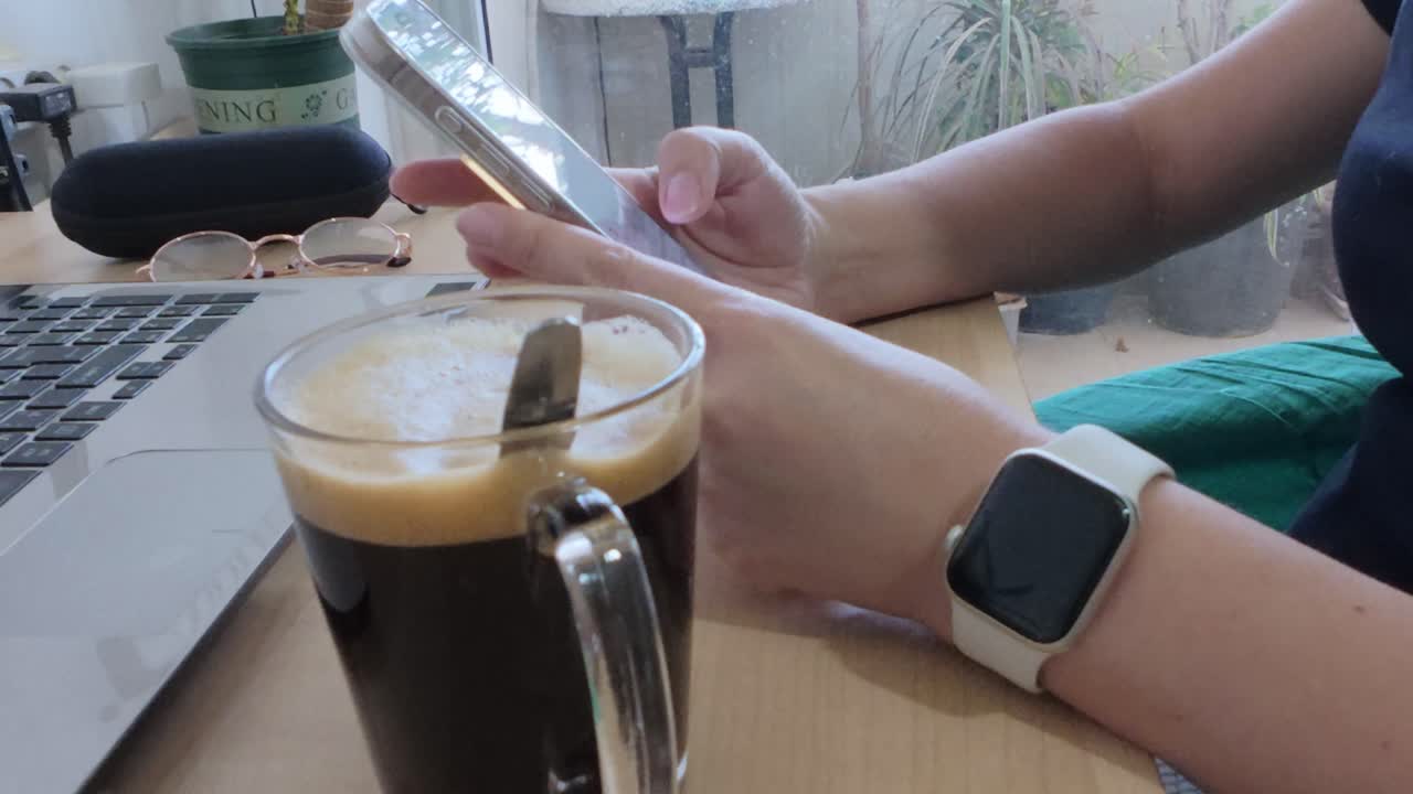 Home office scene: person using phone by laptop and coffee.