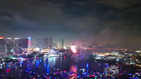 stunning aerial fireworks erupt over the bay as dozens of boats gather below and city lights flicker in the urban nightscape