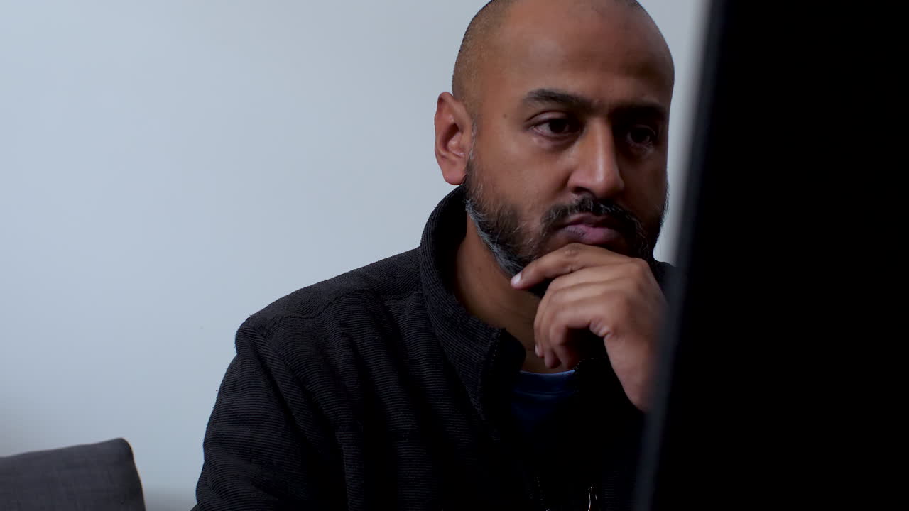 hombre del sur de asia con la mano en la barbilla trabajando pensativamente desde casa en la computadora portátil, contemplando ideas y soluciones