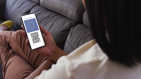 mujer en casa con un teléfono inteligente con certificado de vacunación contra la covid, bandera de la ue y código qr en la pantalla