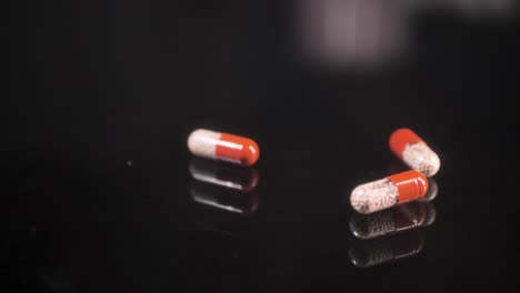 Pills-falling-down-on-a-black-glass-surface,-mirror-surface-with-a-reflection-on-black-background