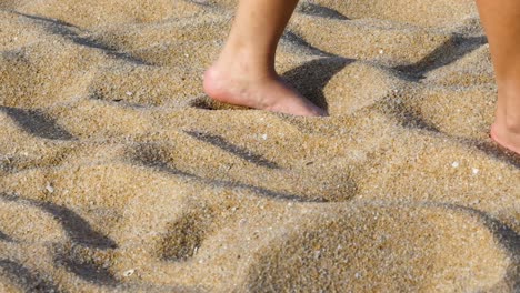 close-up of bare feet walking across sunlit, textured sand, leaving gentle footprints behind.