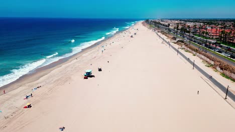 drone flying over huntington beach california with a police car driving down the beach