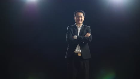 smiling asian speaker man in business suit crossing his arms while standing in the black screen studio