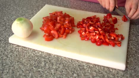 mujer cortando pimiento rojo en una tabla de cortar con rodajas de tomate y cebolla blanca al costado