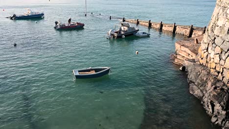 old stone harbour and slipway with small boats bobbing in calm waters on bright sunny day salerie corner,guernsey,but could be anywhere