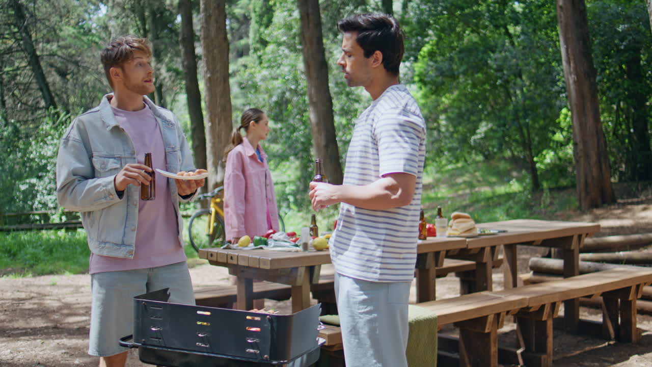 Two men talking picnic with beer in green forest. Group friends communicating