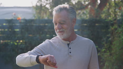 senior hispanic man checking smart watch in garden at home