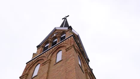 Beautiful-tall-brick-church-with-cross-on-top-and-overcast-clouds-in-the-sky