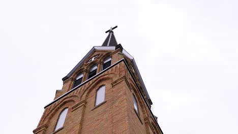 beautiful tall brick church with cross on top and overcast clouds in the sky