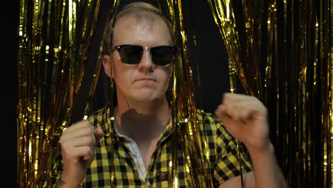 portrait of caucasian man posing on black background. gold shining foil strips. party, music, disco