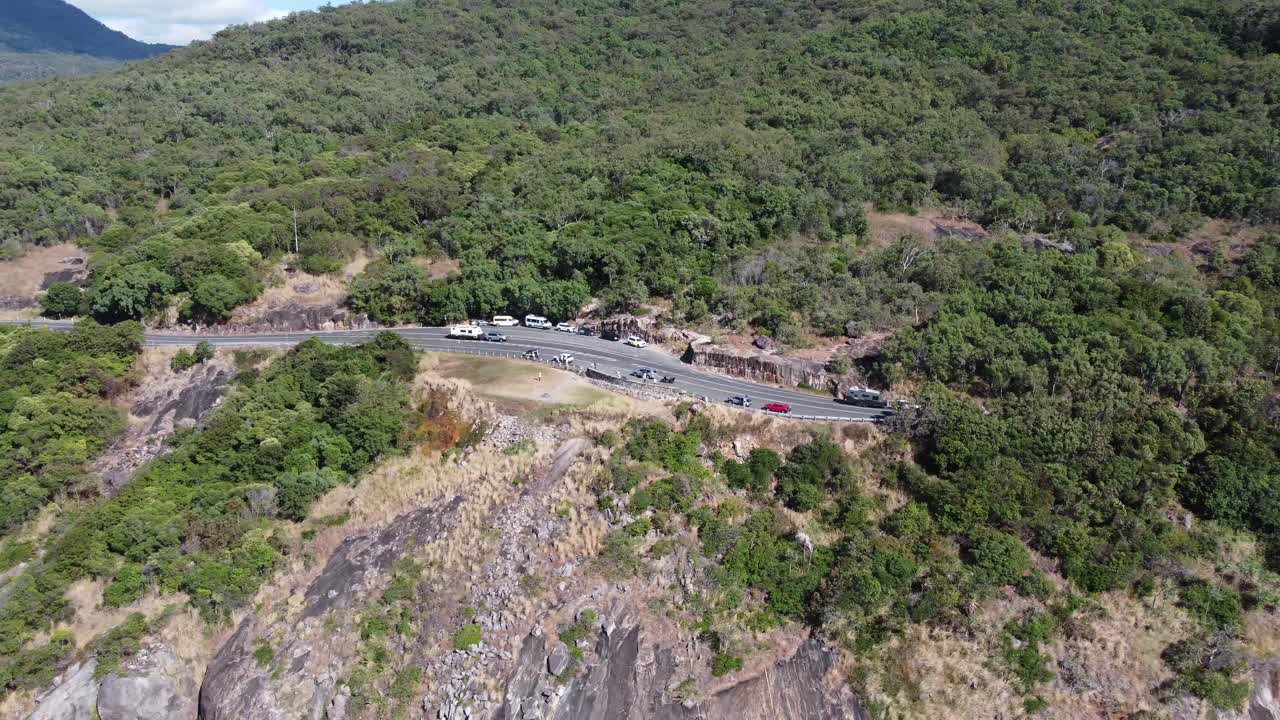 Drone Backing away from a rugged coastline with a cliff and mountains in the background
