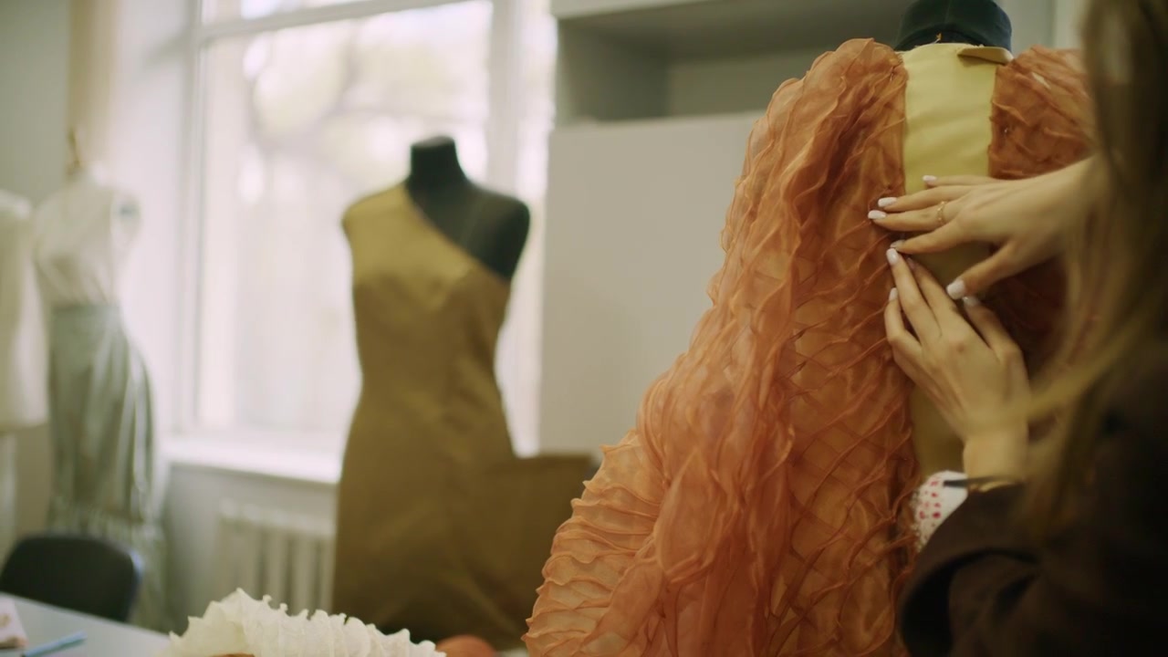 Chisinau, Moldavie - 10 avril 2026 : Les mains d'une créatrice tiennent une pelote à épingles ronde remplie d'épingles de couturière argentées tout en travaillant sur un tissu d'organza orange superposé