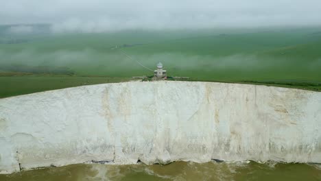 Distant-view-of-Belle-Tout-Lighthouse,-white-cliffs,-green-fields-and-sea-taken-by-dji-mini-3-pro-drone-in-Eastbourne-England