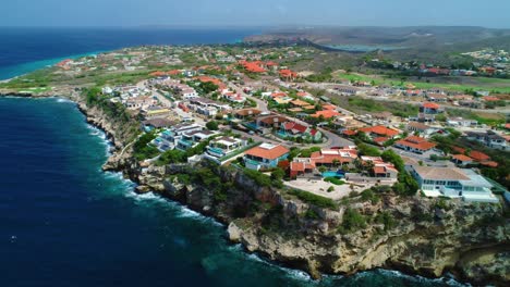 Cloud-shadows-float-across-coastal-villas-overlooking-deep-blue-ocean,-aerial-orbit