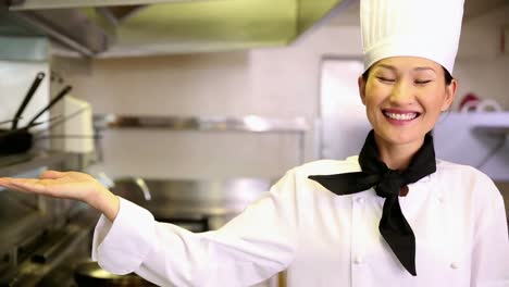 Happy-chef-smiling-at-camera-holding-her-hand-out-in-presentation