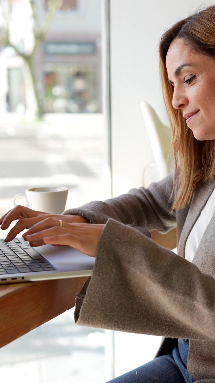 Donna felice che lavora da remoto con il portatile in una caffetteria