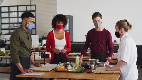 cocinera caucásica que enseña a un grupo diverso usando máscaras faciales