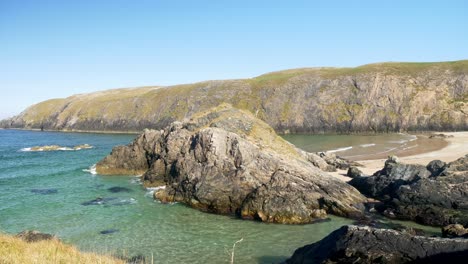 Timelapse-of-a-sandy-beach-with-large-rocks-in-the-foreground-and-a-barren-headland-in-the-distance