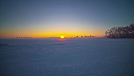 bright, golden sunrise on a hazy, winter day with no clouds across a field of snow - time lapse