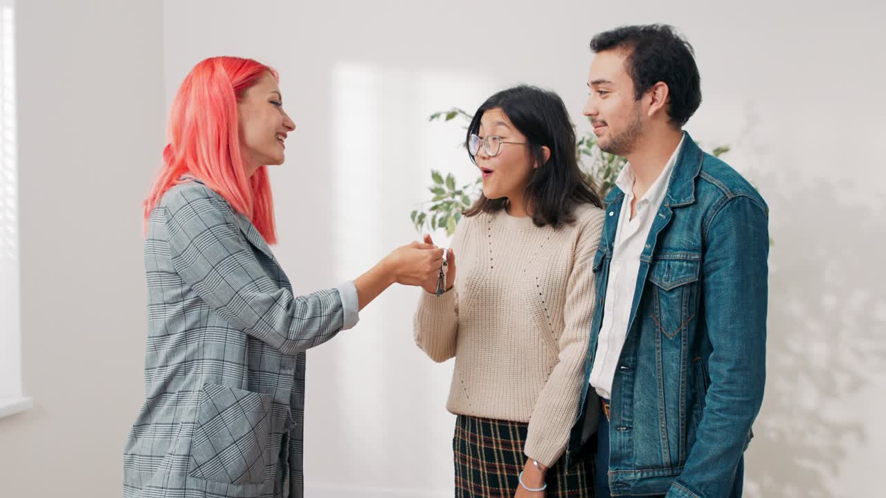 Seorang agen properti menyerahkan kunci apartemen yang baru dibeli kepada pasangan muda yang sedang jatuh cinta. Wanita itu sangat gembira menerimanya, dia dengan senang hati memeluk pacarnya sambil tersenyum, dan pacarnya memeluk serta mengangkatnya.