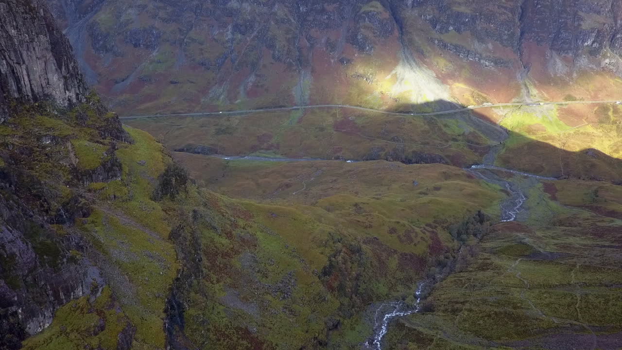 el vuelo desciende por un valle rocoso verde hacia el tráfico en una carretera sinuosa